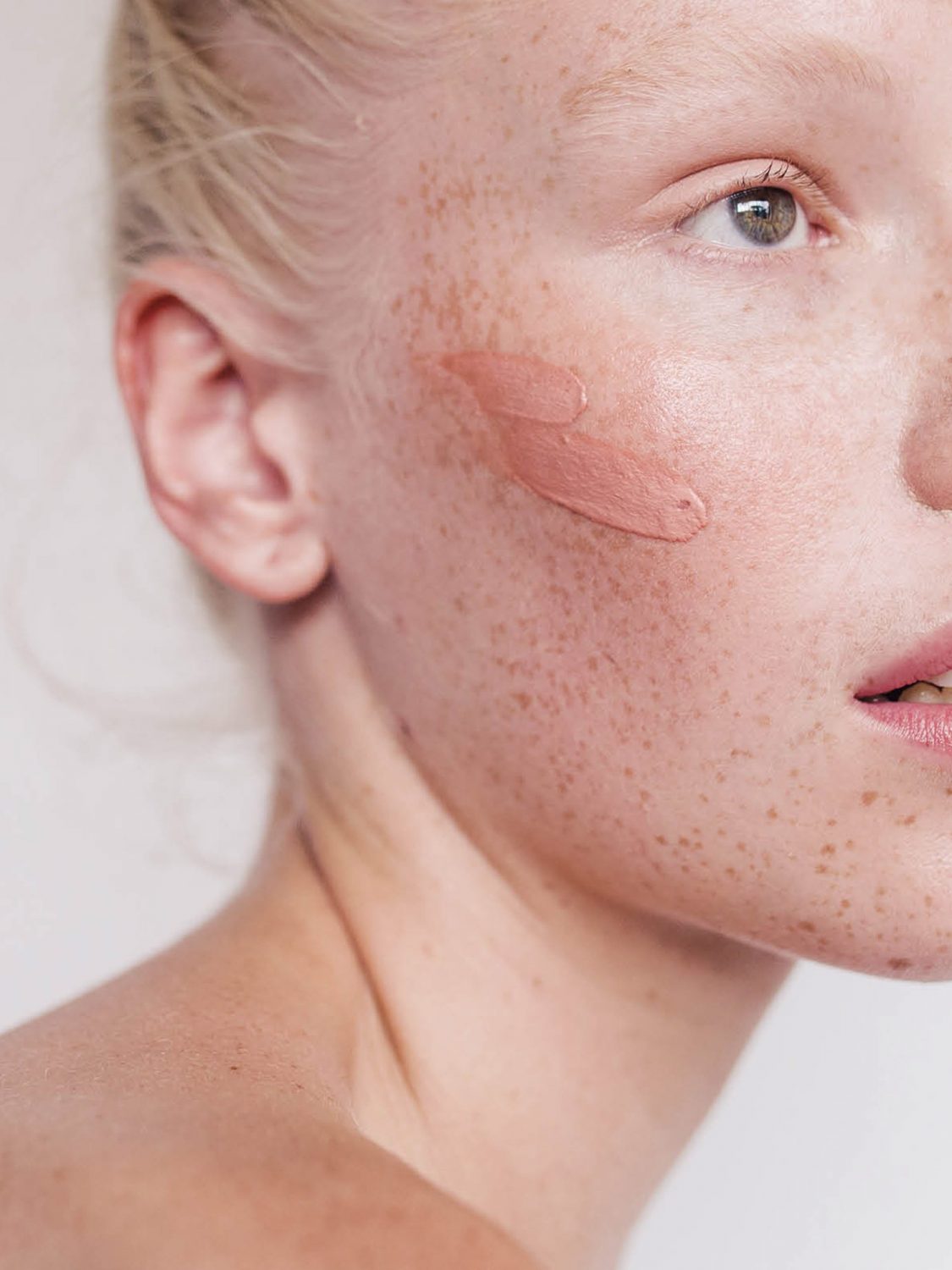Gesicht einer Frau mit Sommersprossen, auf der Wange sieht man Make Up